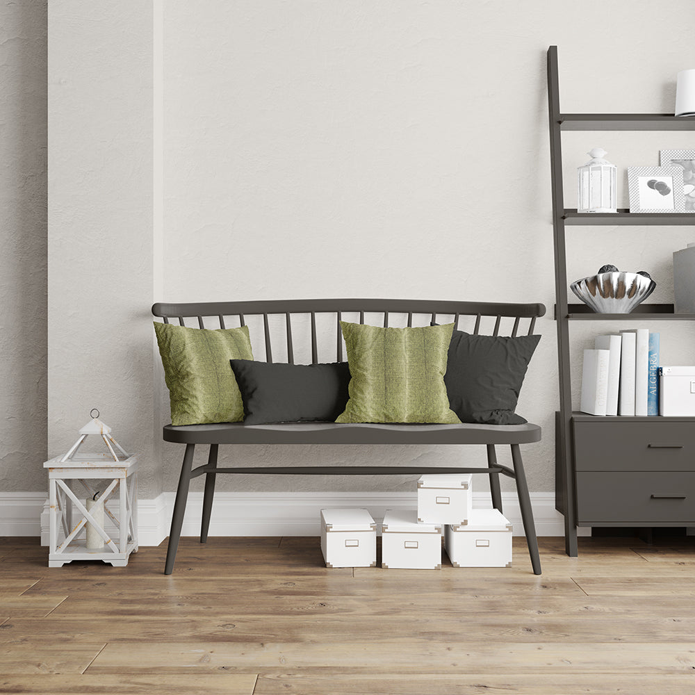 Dark gray metal-framed bench with olive green and charcoal cushions on a wooden floor, white storage boxes beneath, and a dark shelving unit with books.