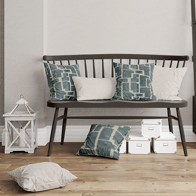 Gray wooden bench with slatted back and tapered legs, teal geometric pillows and white cushions, lantern and white boxes.