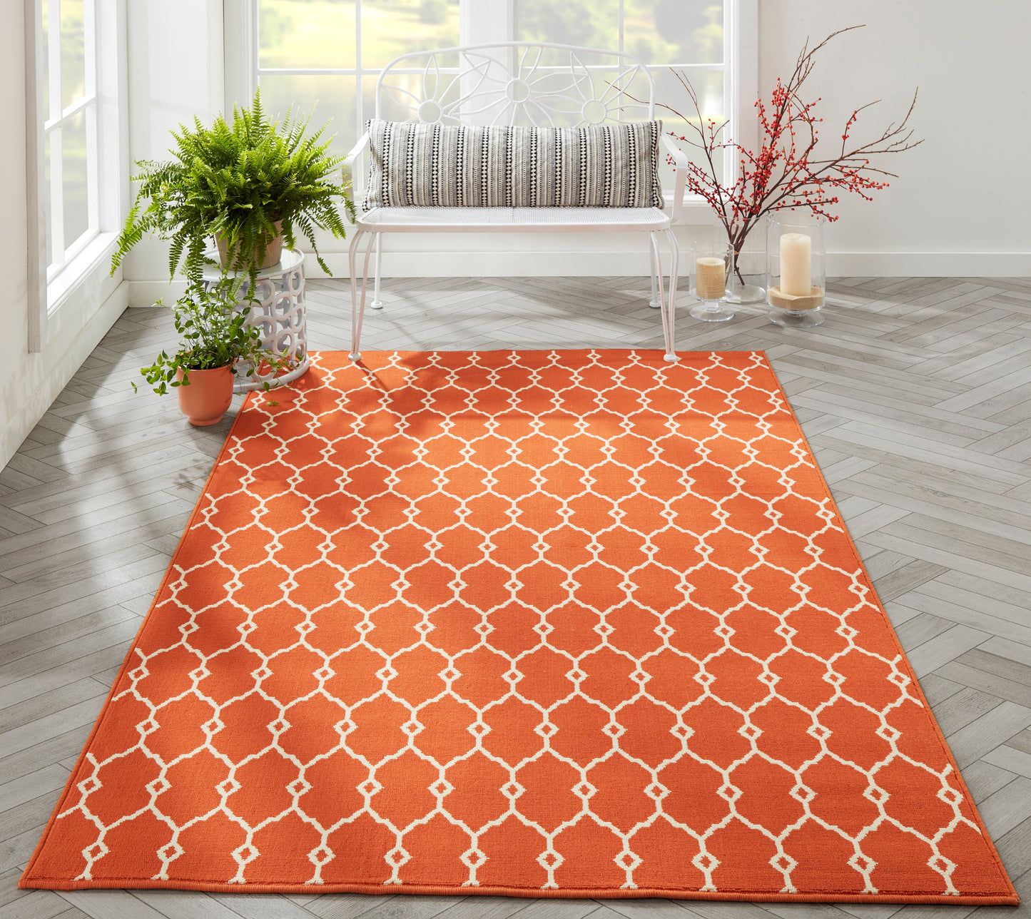 Orange rectangular rug with white trellis pattern in a bright living room, paired with a white bench, potted plant, and candles.