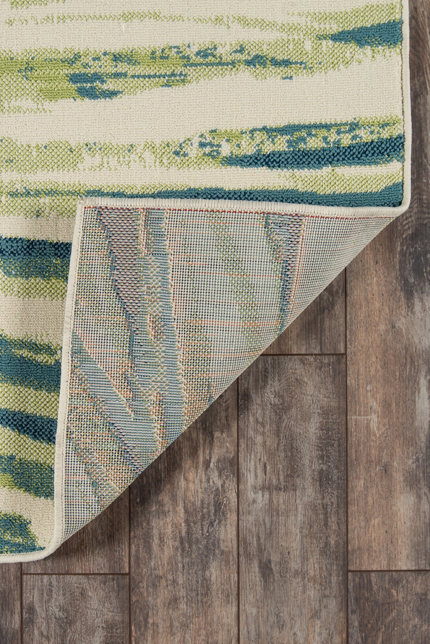 Green and blue abstract striped rug with a white edge, folded to show light blue backing on a wood floor.