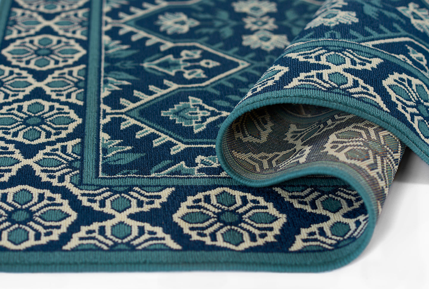 Turquoise and navy geometric woven rug with white motifs; rolled edge reveals contrasting underside.