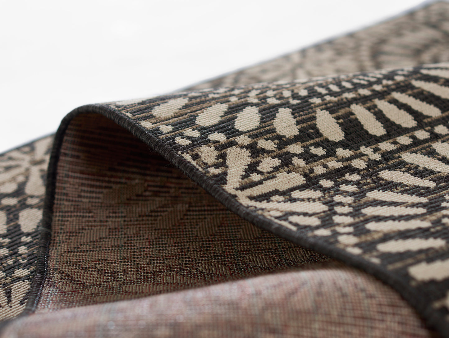 Close-up of a woven Baja rug with black & beige geometric pattern; folded edge reveals dense brown underside.