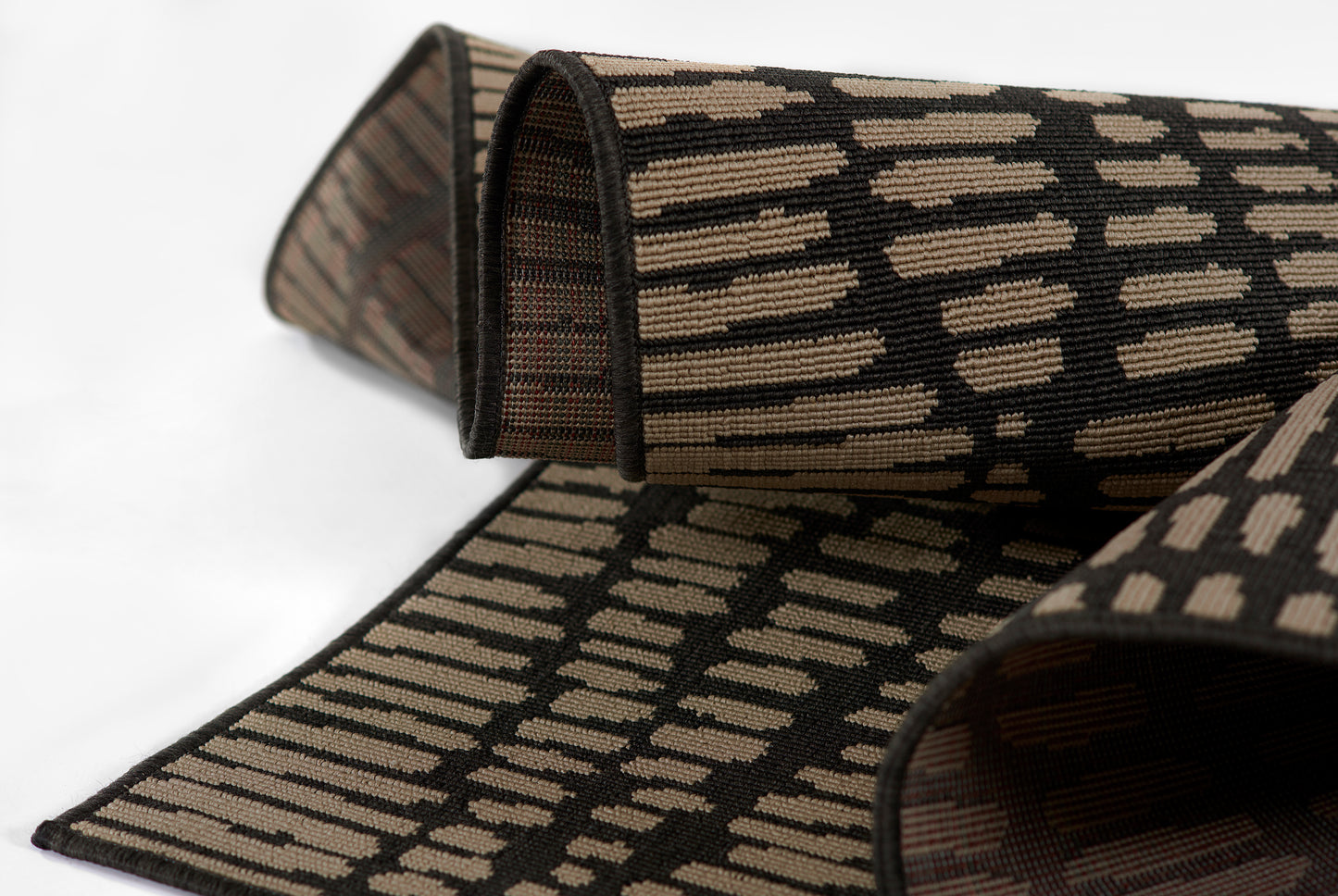 Rolled woven rug with tan geometric panels on black; kilim-inspired rug for home decor.