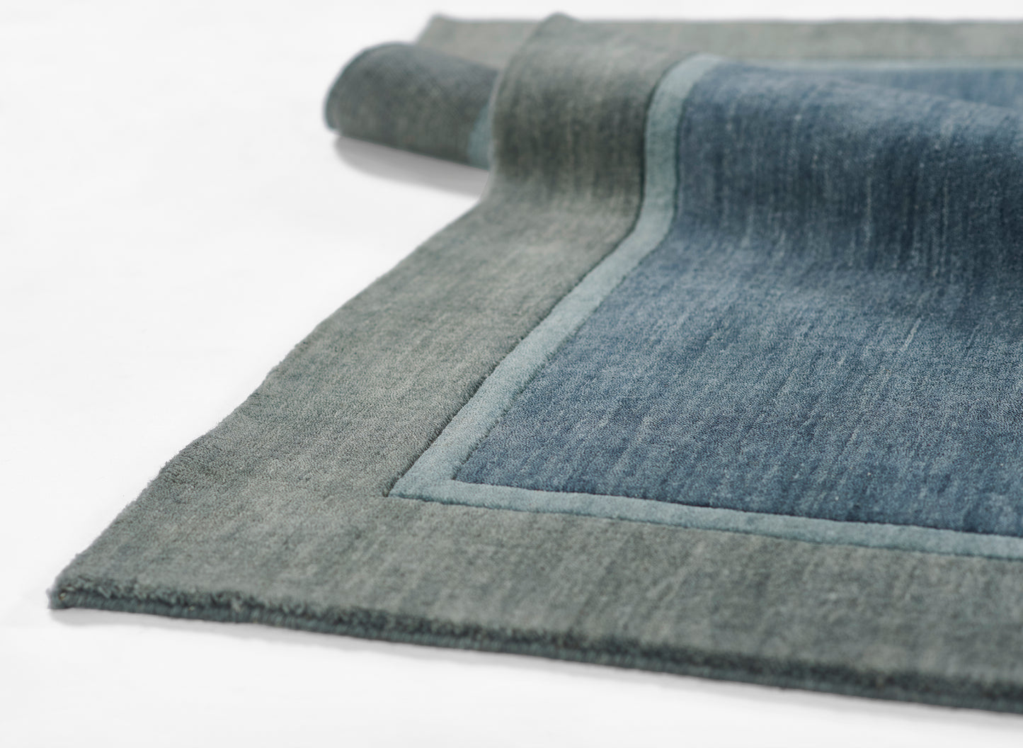 Rectangular rug with grey border & blue denim center, soft pile, blue piping along edge, rolled corner.