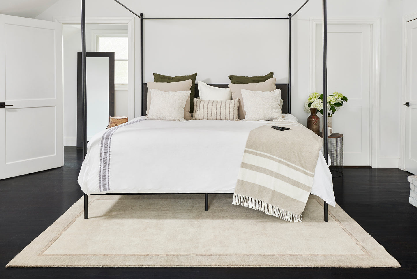Black metal canopy bed with white bedding, beige throw, & neutral pillows in a bright modern bedroom.