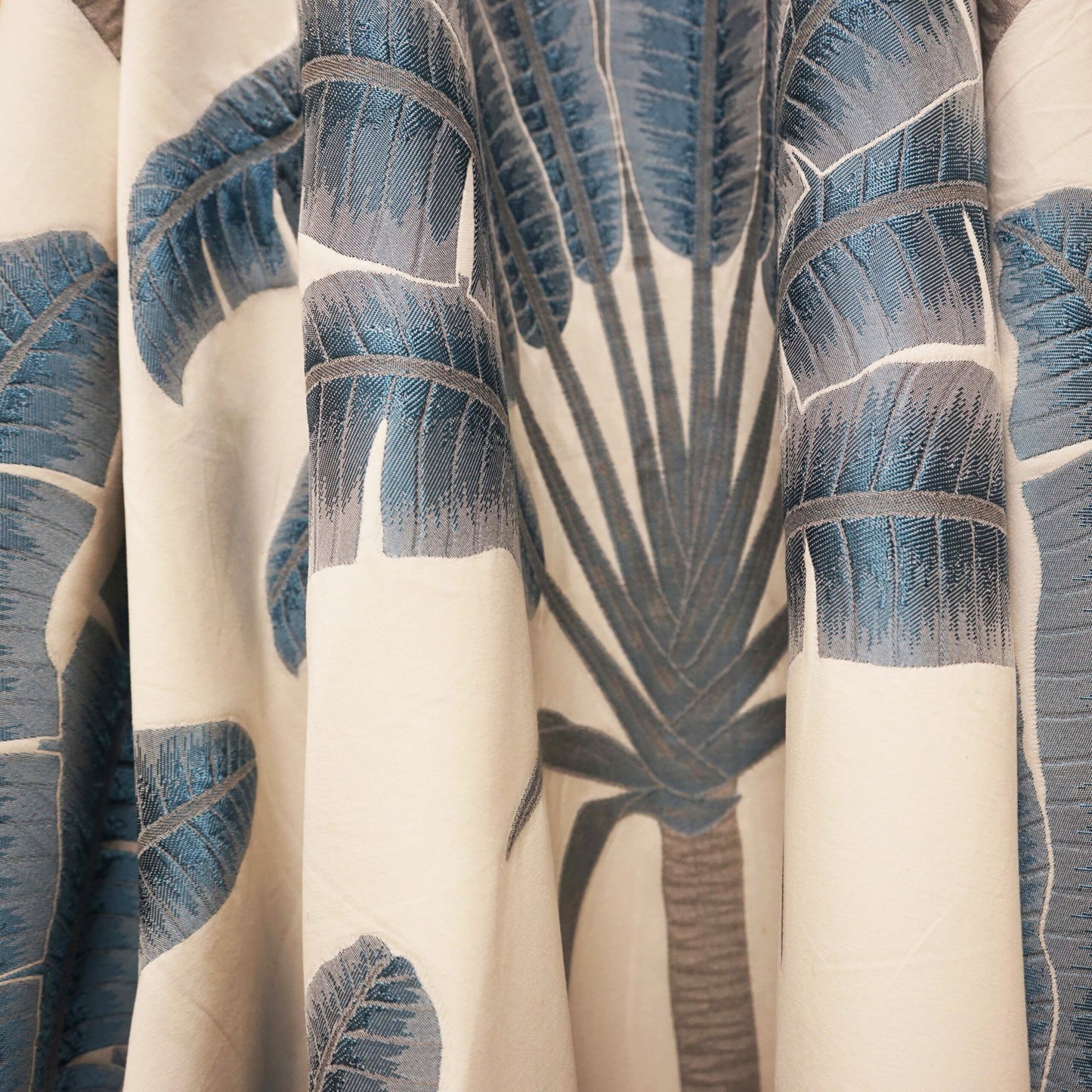 Cream fabric with blue palm leaf print, tropical botanical pattern, soft drape, ideal for curtains or throws.