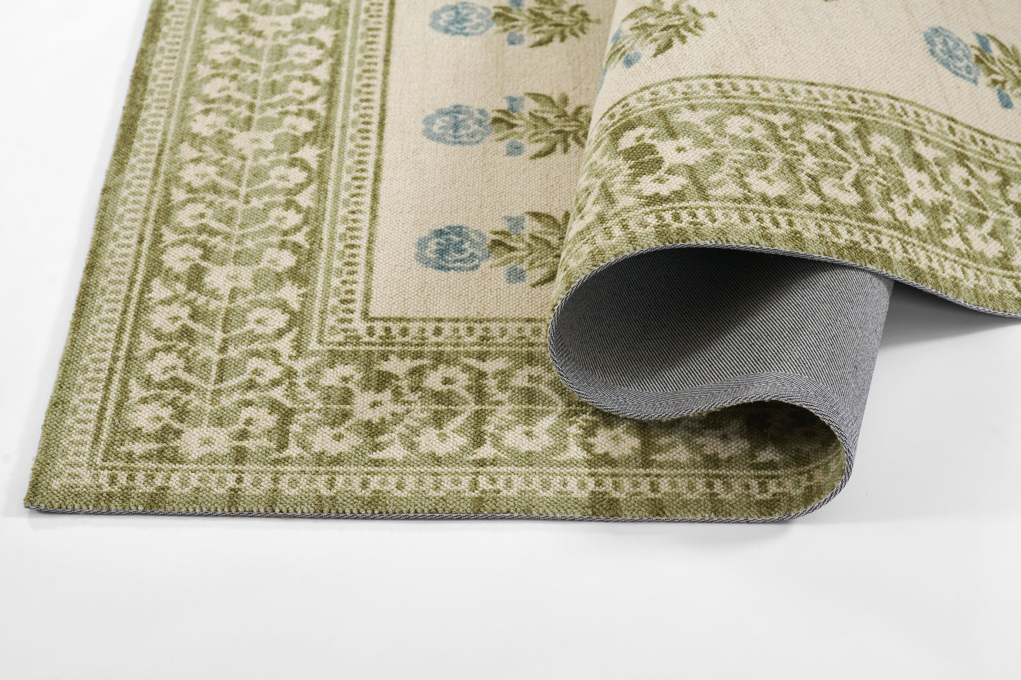 Olive green border rug with cream field and blue floral accents; woven textile, rolled corner shows gray underside.