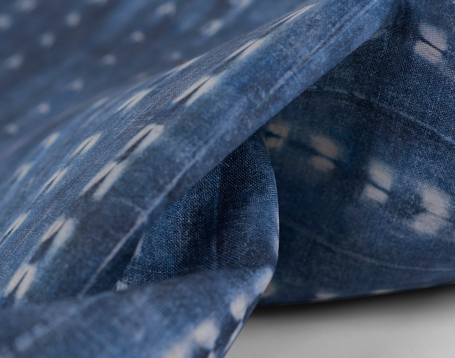 Close-up of blue denim fabric with faded white specks and folded edge.