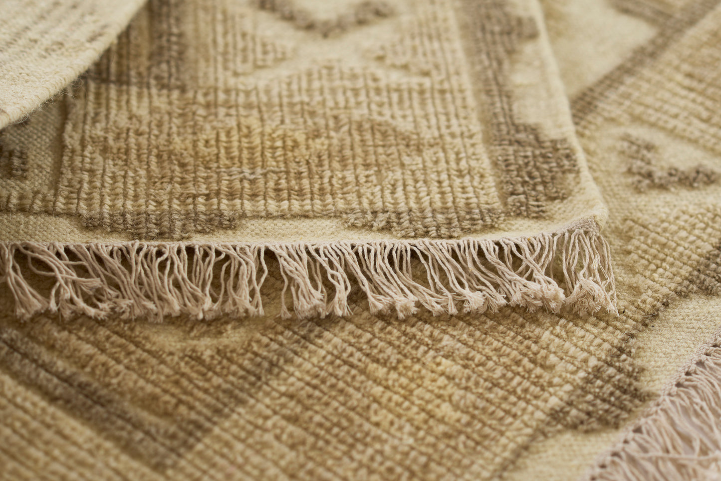 Natural beige woven rug with fringe trim and textured geometric pattern; rustic boho style for living room or entry.