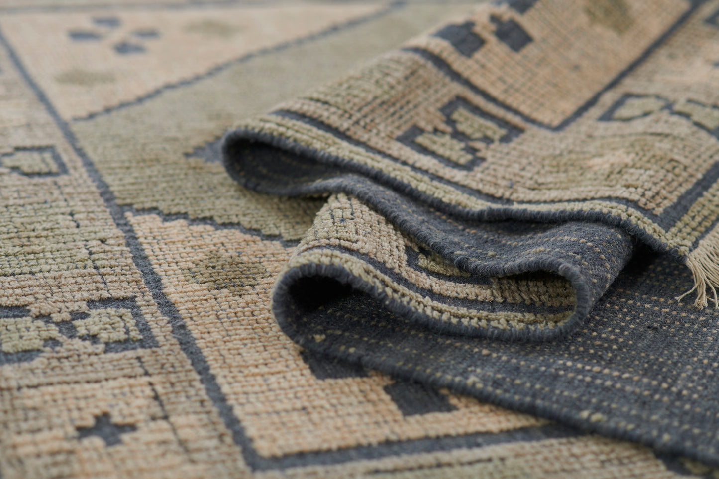 Beige and navy geometric woven rug, rolled edge showing textured pattern and dark underside.