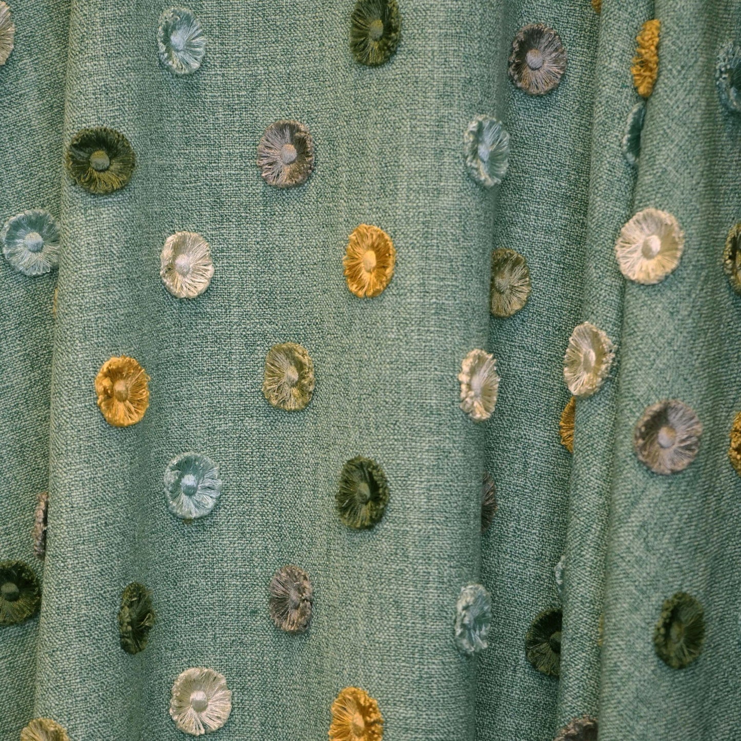 Teal woven fabric with scattered multicolor circular button-like embroidery patches in blues, greens, yellows.