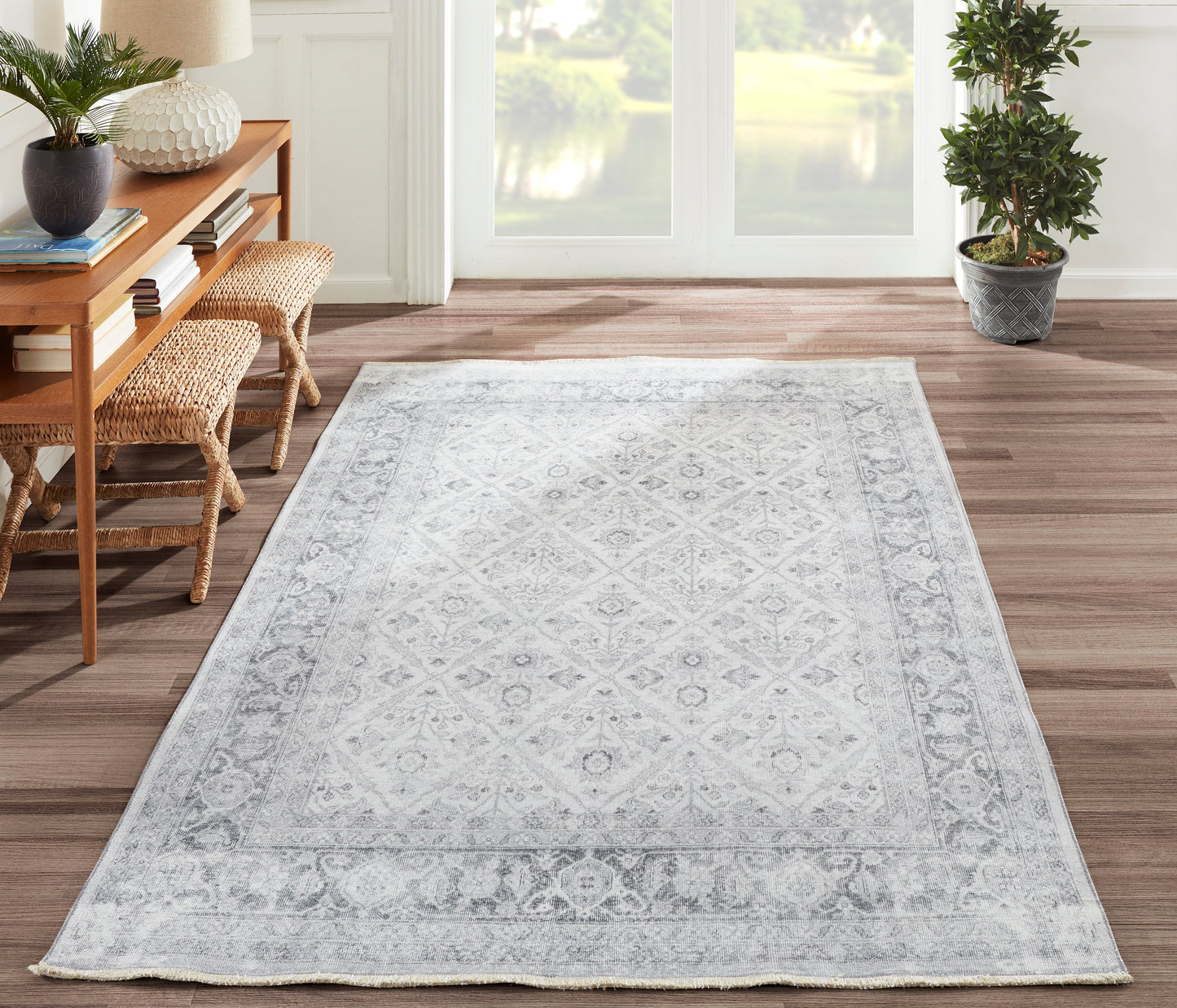 Light gray patterned area rug with ornate border on a wooden floor, paired with a wooden console and potted plants.