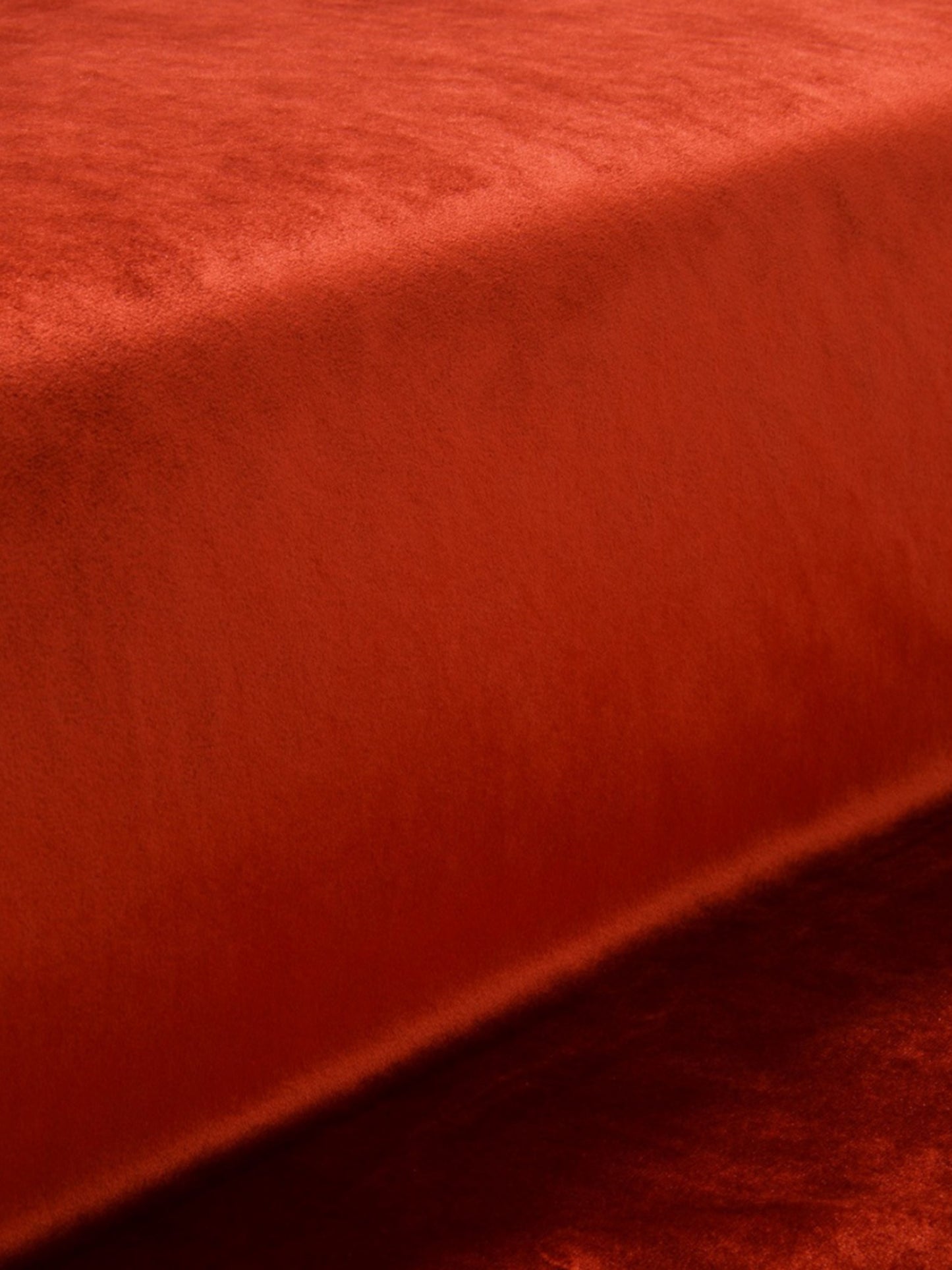 Orange-red velvet bed throw draped over mattress edge, rich texture and cozy style.