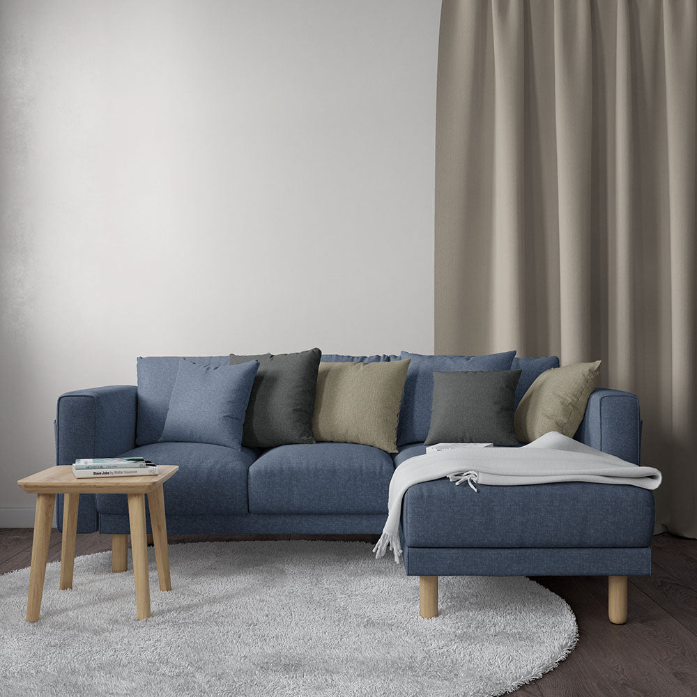 Blue solid fabric sectional with chaise, light wood legs, blue/gray/olive cushions, cream throw, small wood coffee table, gray rug.