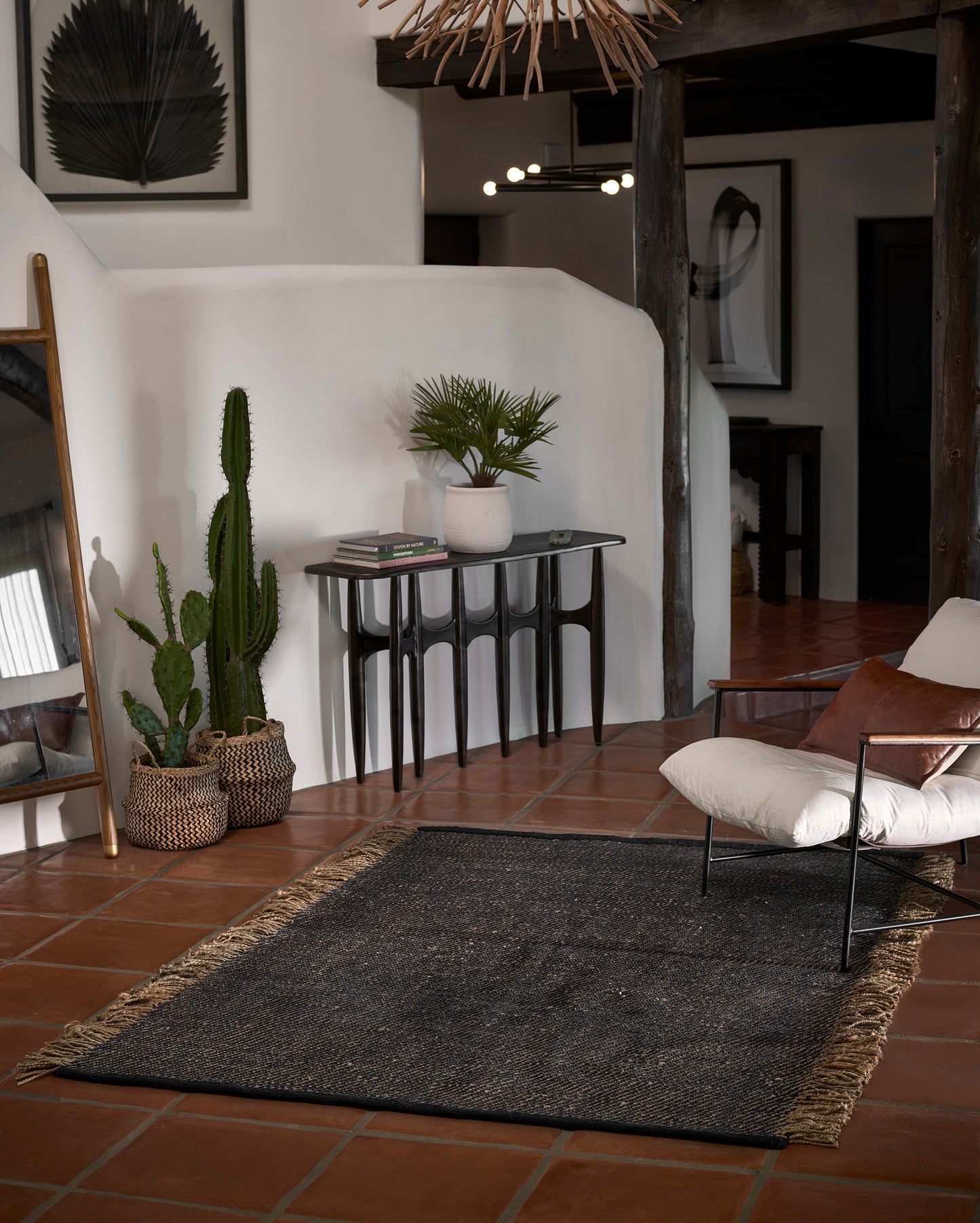 Cozy boho living room with dark fringed rug on terracotta tile, white curved wall, console table with a potted palm and cactus.