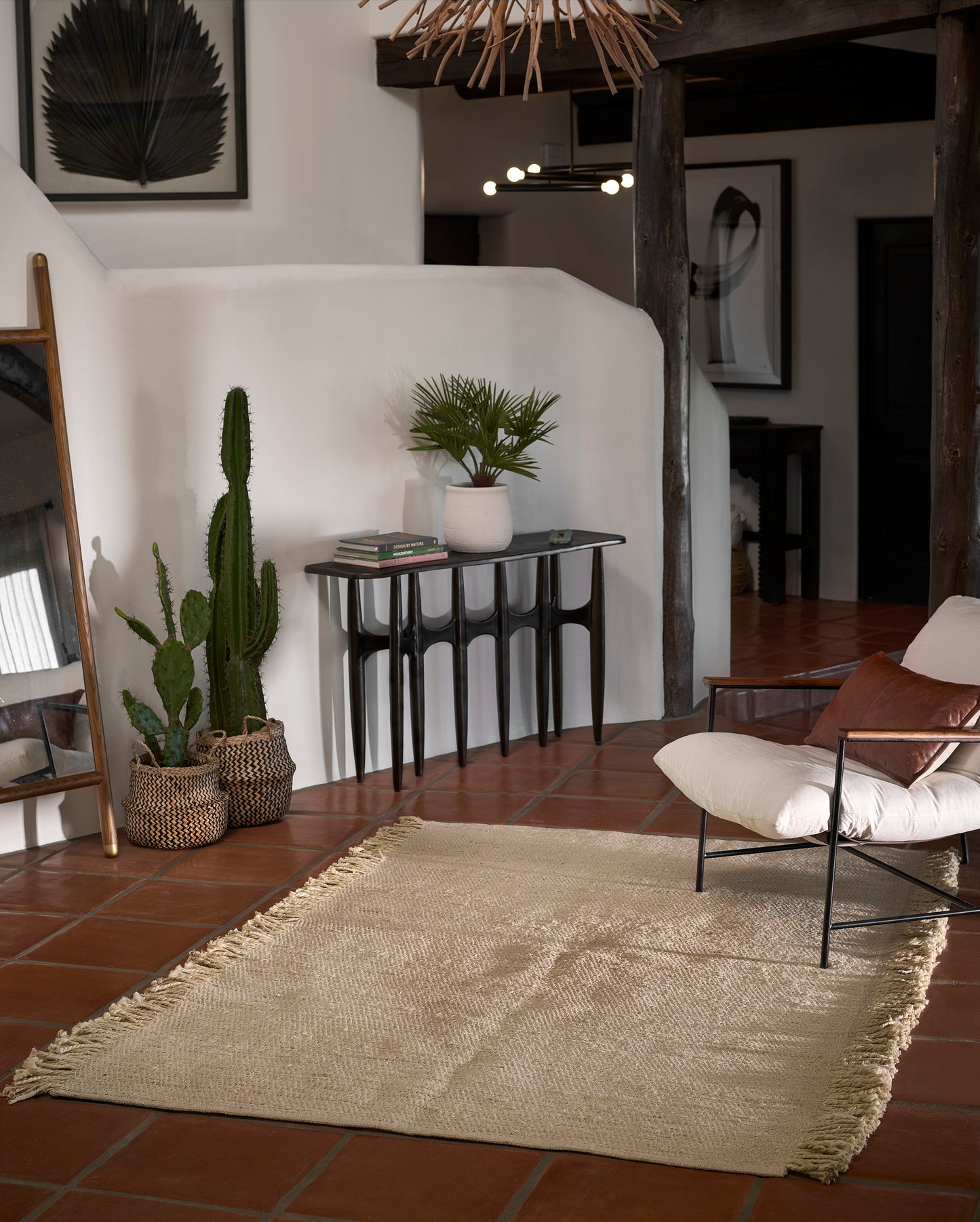 Boho living room with natural jute rug, terracotta tile floor, tall cactus planters, and a console table with potted plants.
