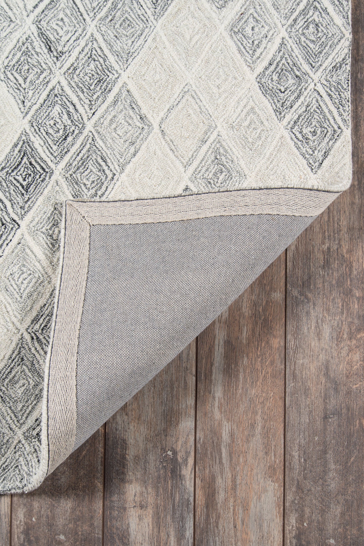 Grey geometric diamond rug with light and dark tones, folded corner reveals backing on wooden floor.