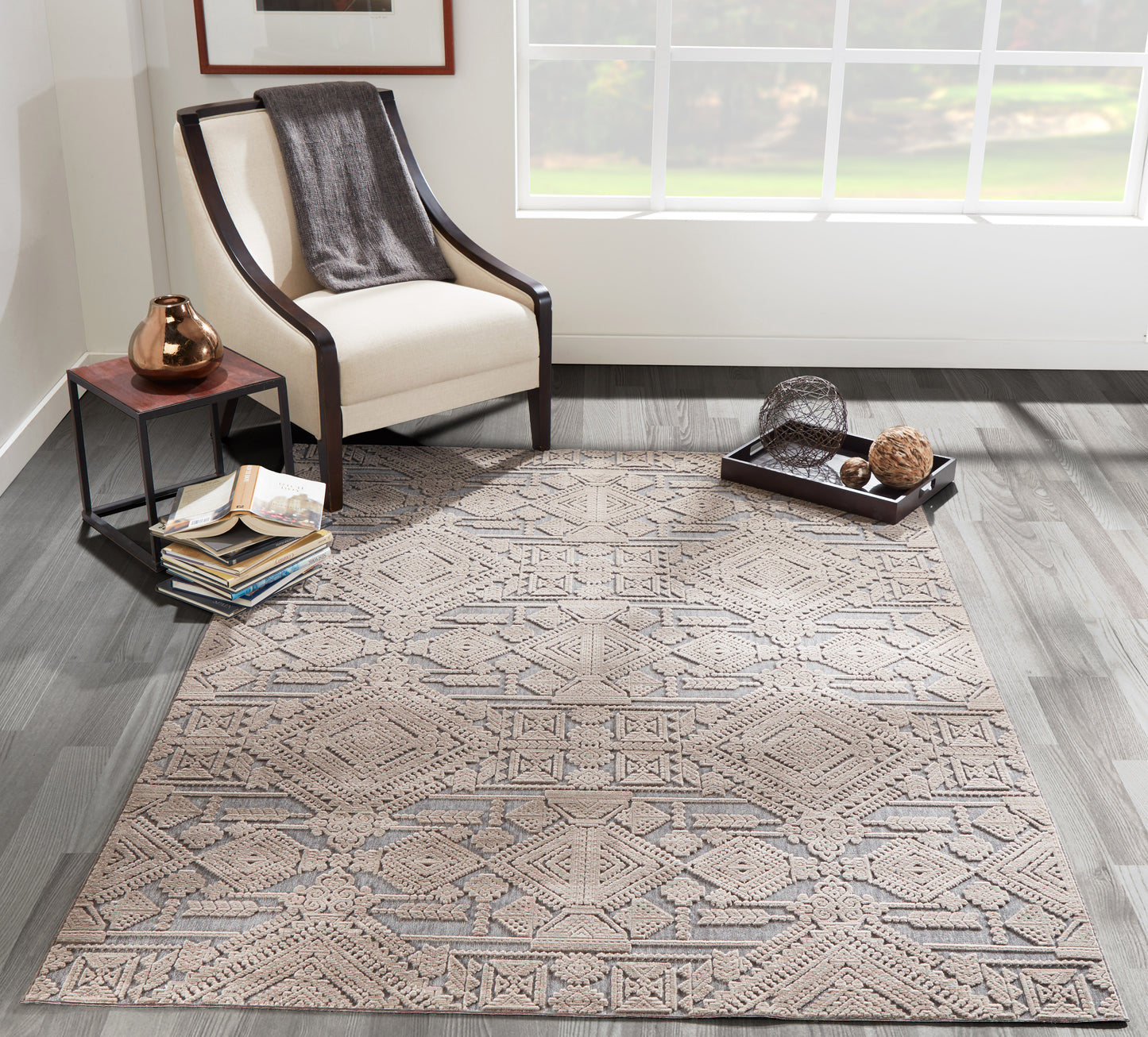 Geometric beige-gray area rug in a living room with a white-armchair, dark wood frame and copper vase on a side table.