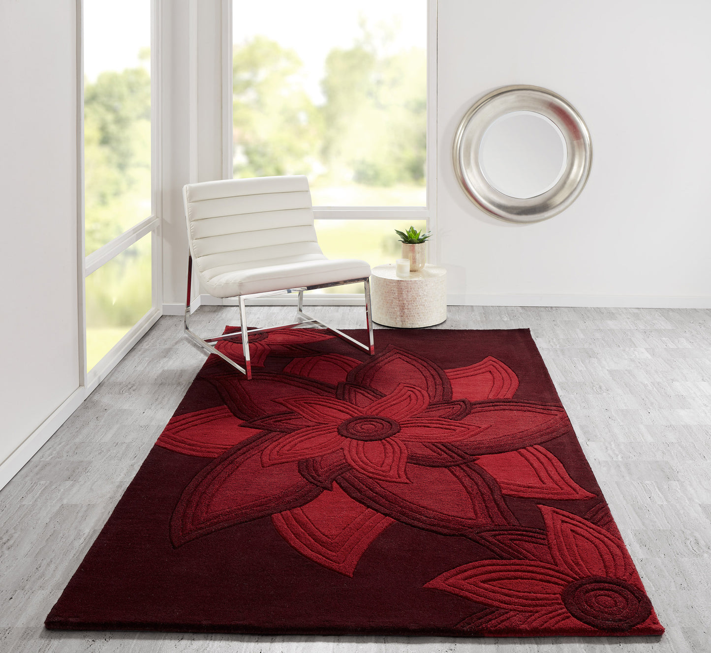 Rectangular burgundy rug with an oversized red floral motif in a bright modern living room beside a white chair.