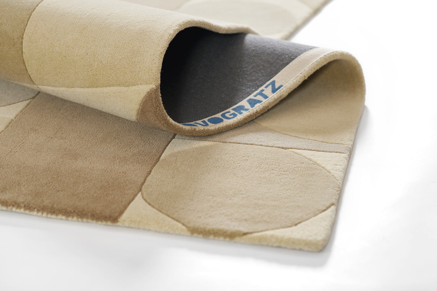 Beige patchwork rug with circular shapes, soft wool-blend, rolled corner.