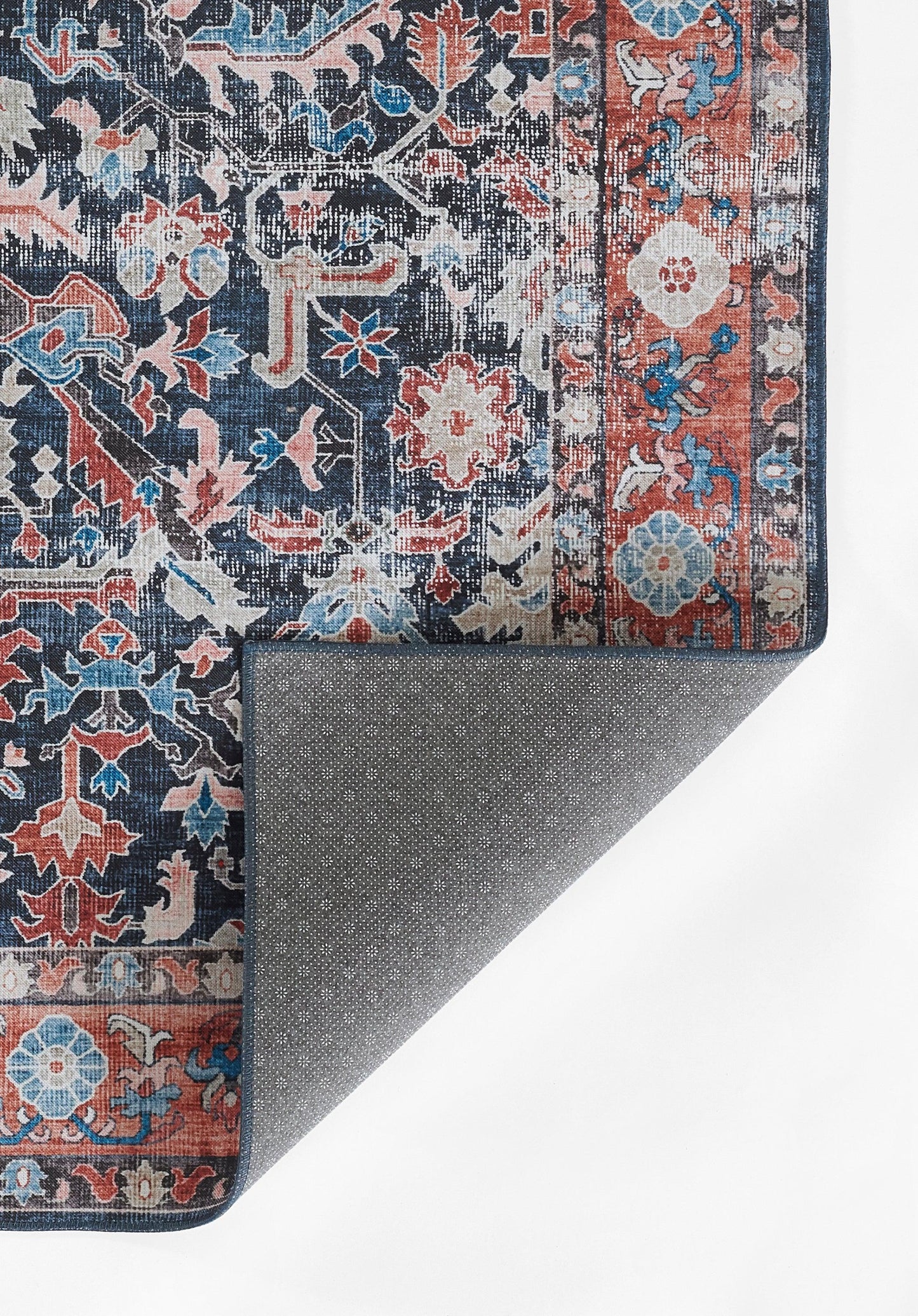 Persian-style rug with navy field, red border and ivory-blue florals; corner folded to reveal grey dotted underside.