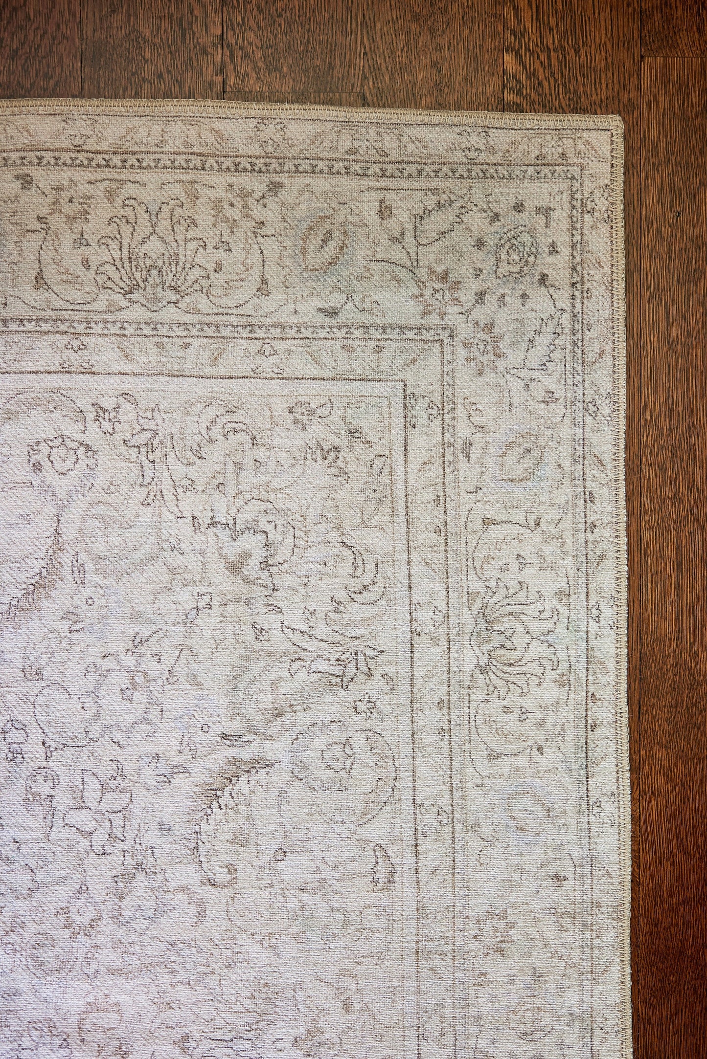 Rectangular soft gray traditional rug with delicate floral border on a dark wood floor.