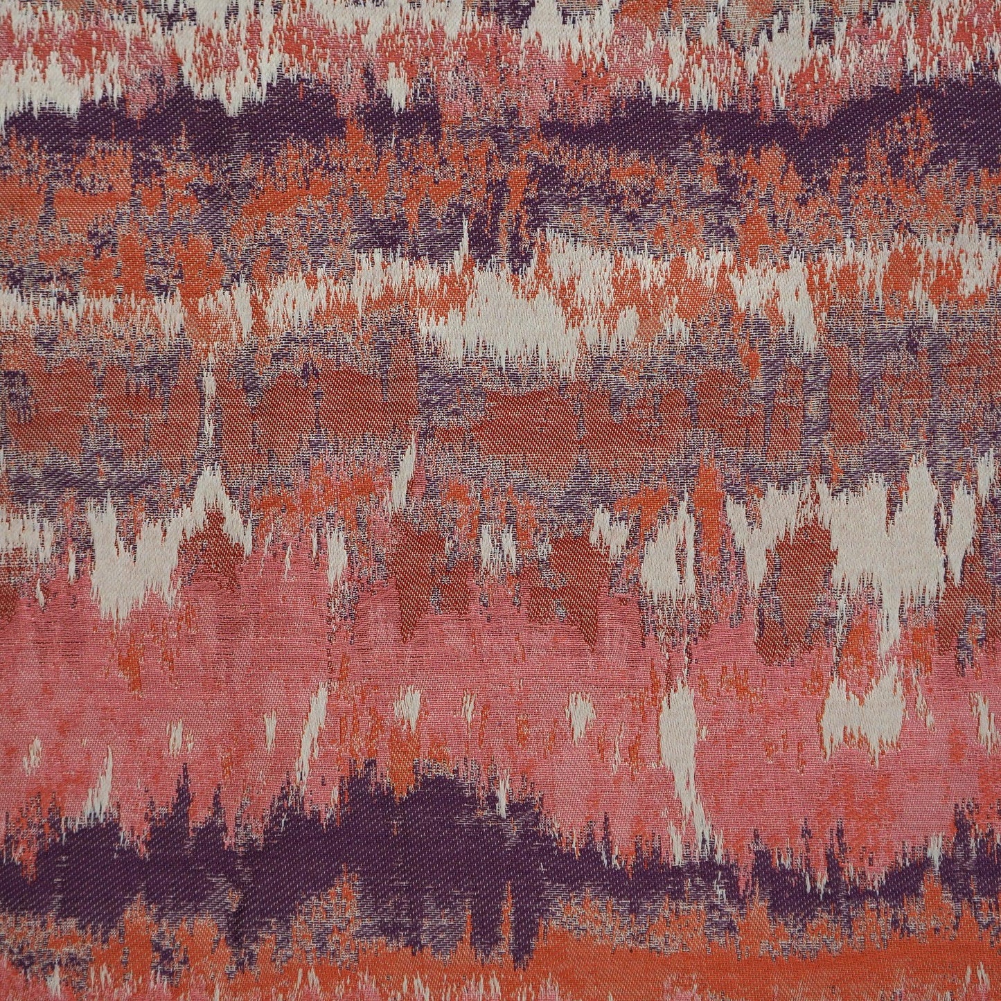 Ikat-style fabric in coral pink, burnt orange, purple and cream with jagged horizontal bands.