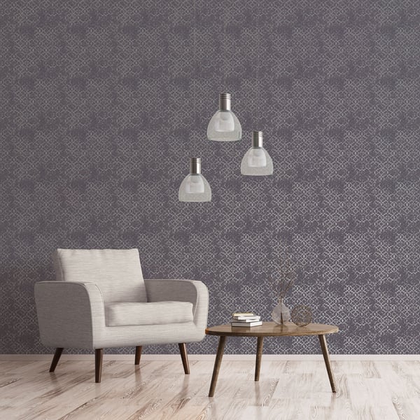 Light gray fabric armchair with wooden legs, round coffee table, patterned wallpaper, and three metal dome pendant lights.