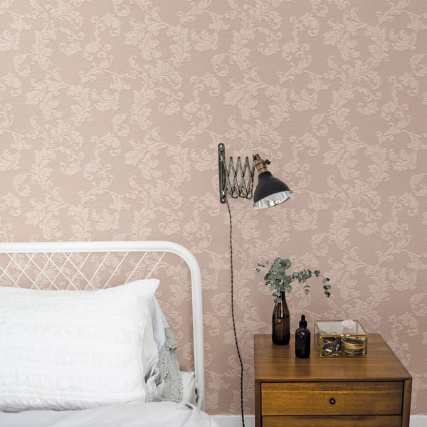 Beige damask wallpaper, white metal bed frame, vintage black swing-arm lamp, and wooden nightstand with vase and bottles.