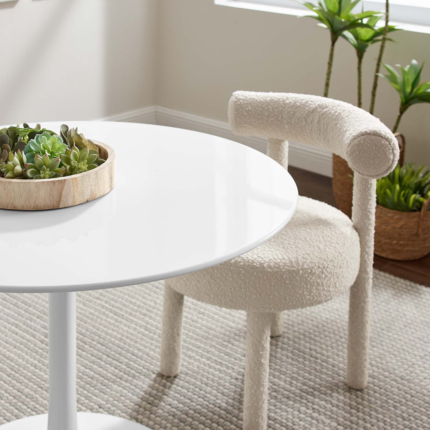 White round table with glossy surface; cream boucle chair; wooden tray of succulents and potted plants.
