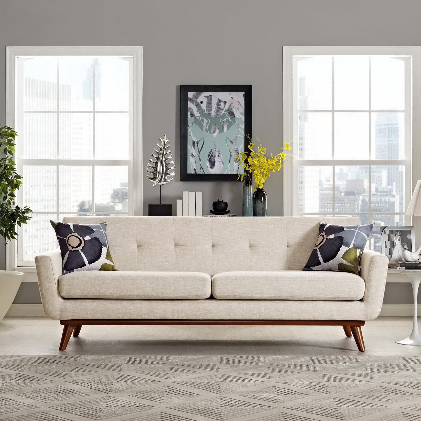 Beige mid-century sofa with tufted back and wooden legs in a gray-walled living room with floral throw pillows.