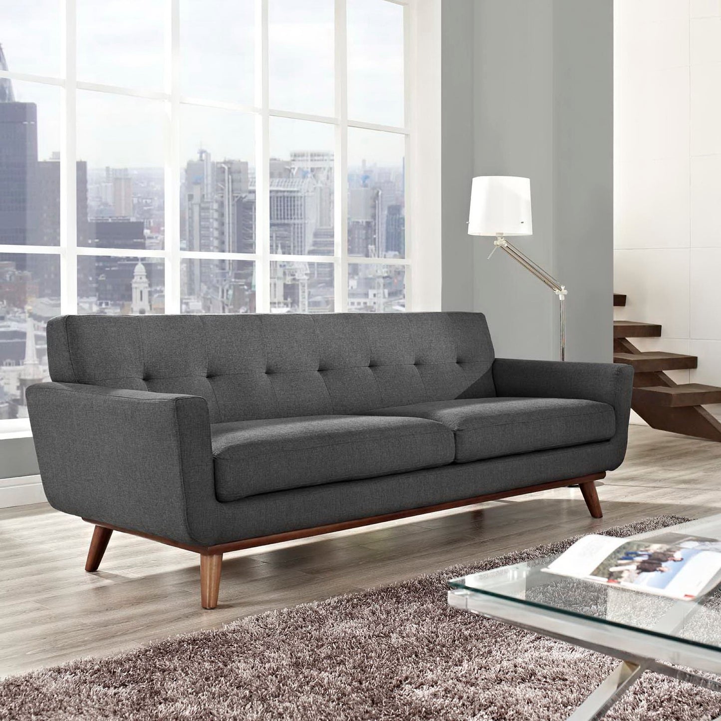 Dark gray mid-century modern sofa with tufted back cushions and wooden legs in a bright living room.