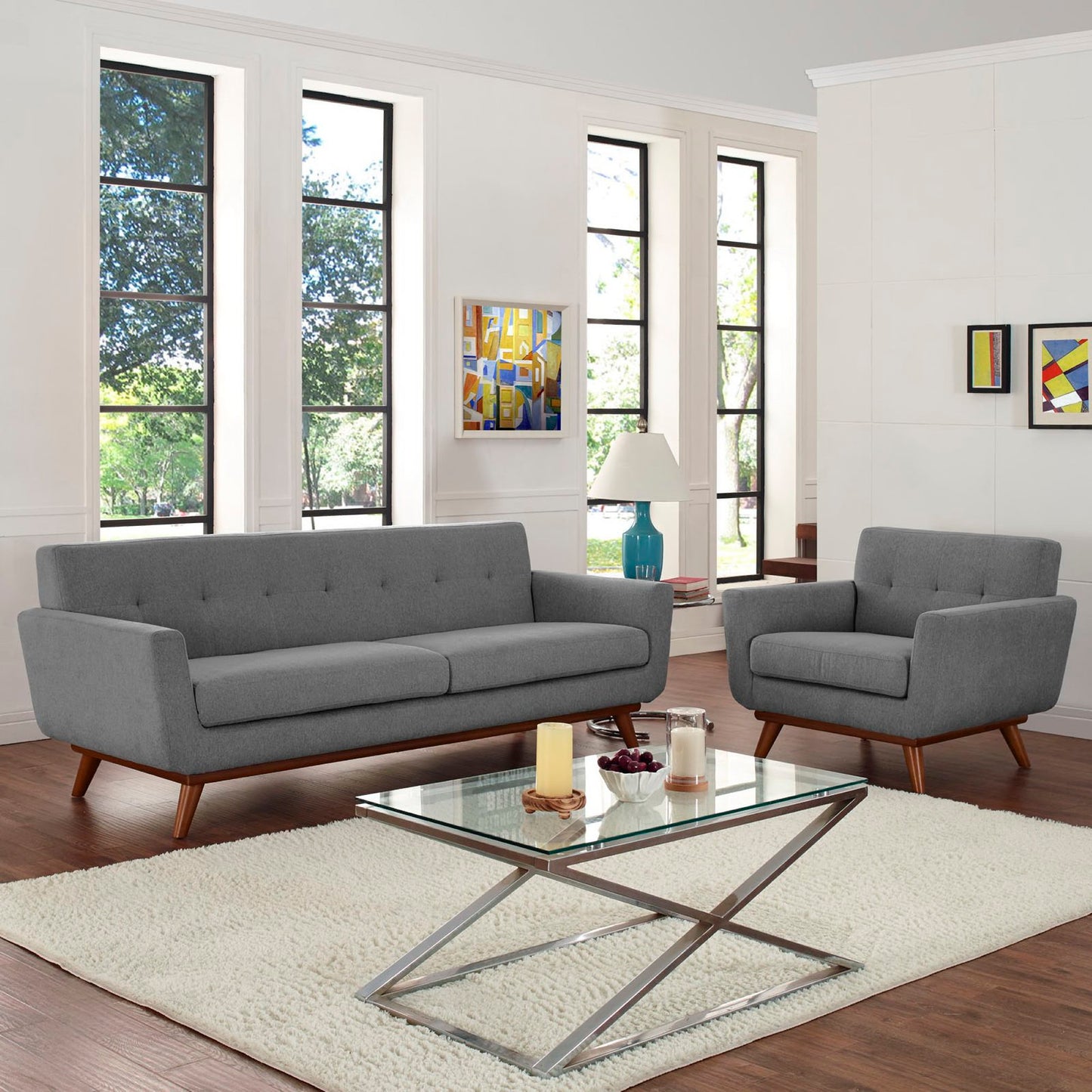 Gray mid-century sofa and armchair with wood legs in a bright living room, glass coffee table with metal X-base