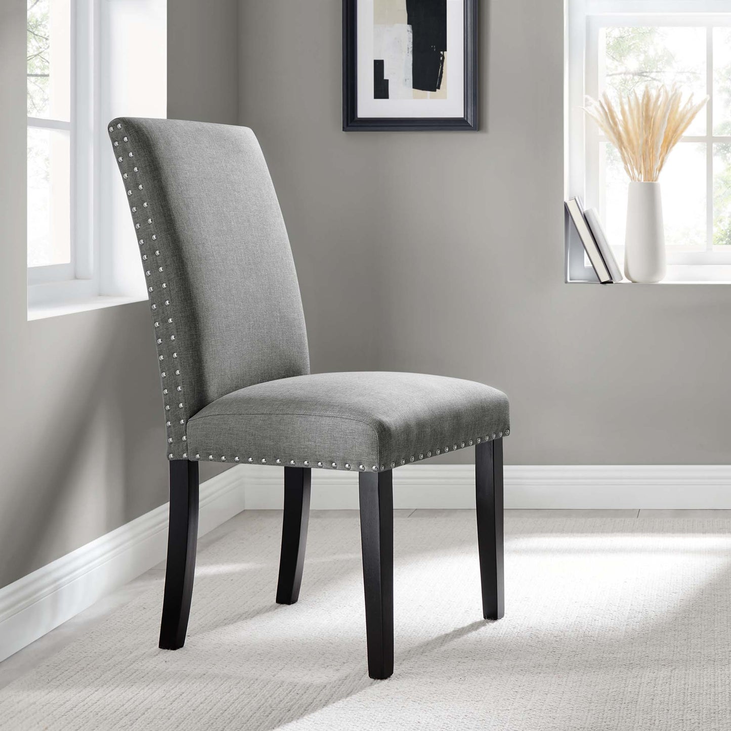 Grey upholstered dining chair with tall back, nailhead trim, and dark curved wood legs.