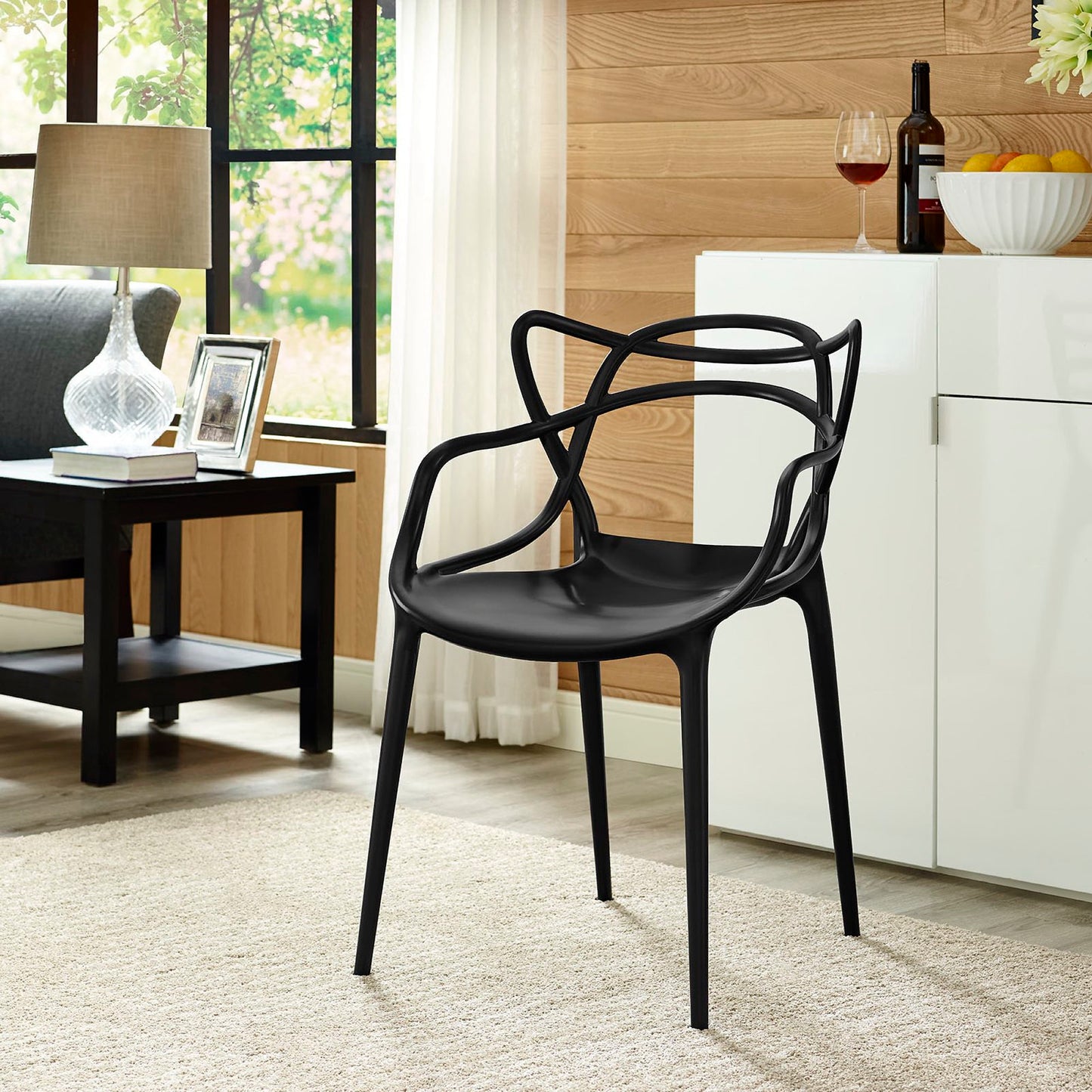 Black molded plastic chair with sculptural open-back curves, four slim legs in a modern living room.