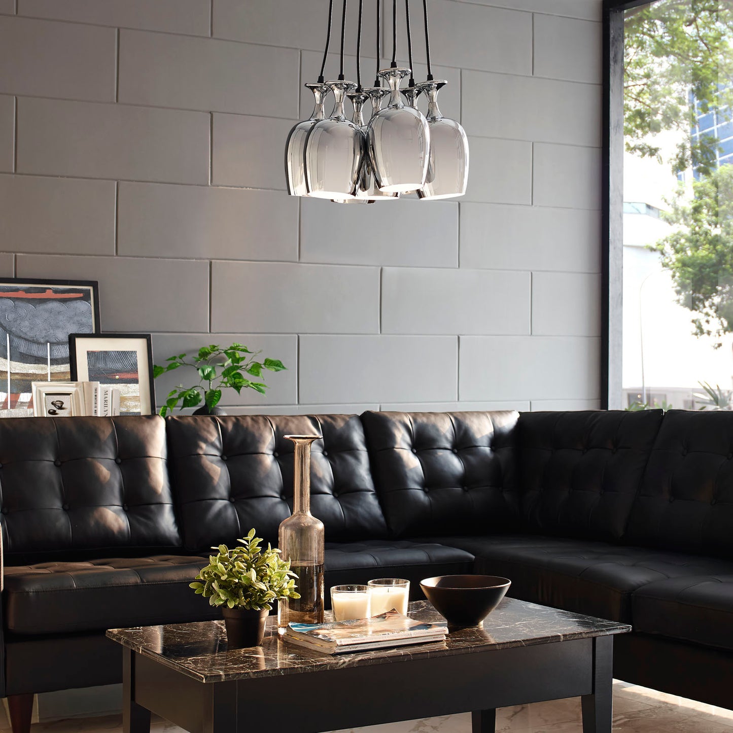 Marble-top coffee table with dark frame in a modern living room; black tufted sectional, glass pendant lights, and greenery.