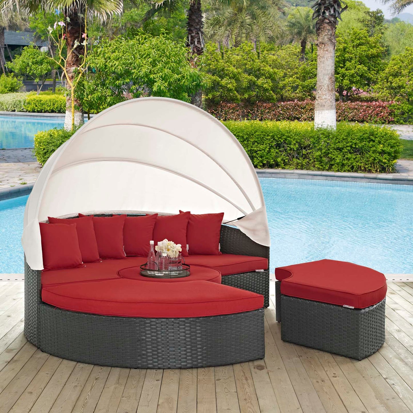 Poolside circular gray wicker outdoor daybed with red cushions, beige canopy, and matching ottoman