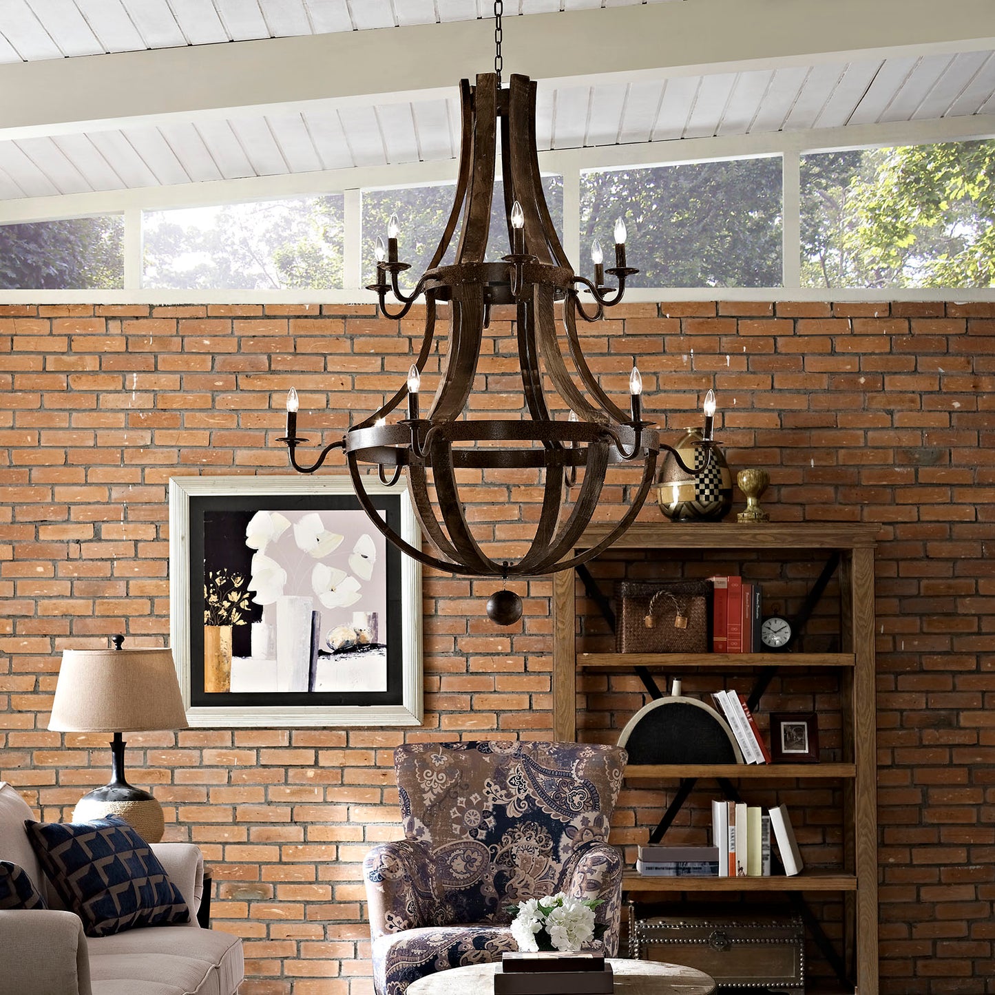 Rustic brown metal chandelier with candle bulbs hanging over a brick-walled living room above a patterned chair and bookcase
