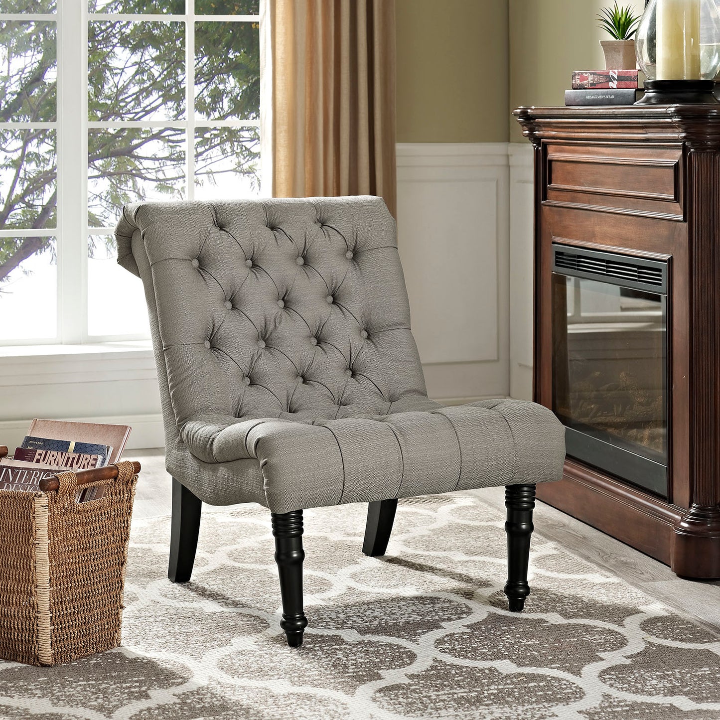 Gray fabric lounge chair with dark turned legs in a living room beside a wood fireplace