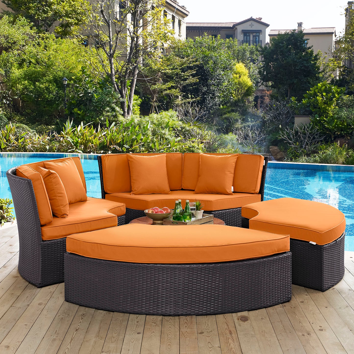 Outdoor wicker modular sectional with bright orange cushions, curved ottoman, and round coffee table poolside.