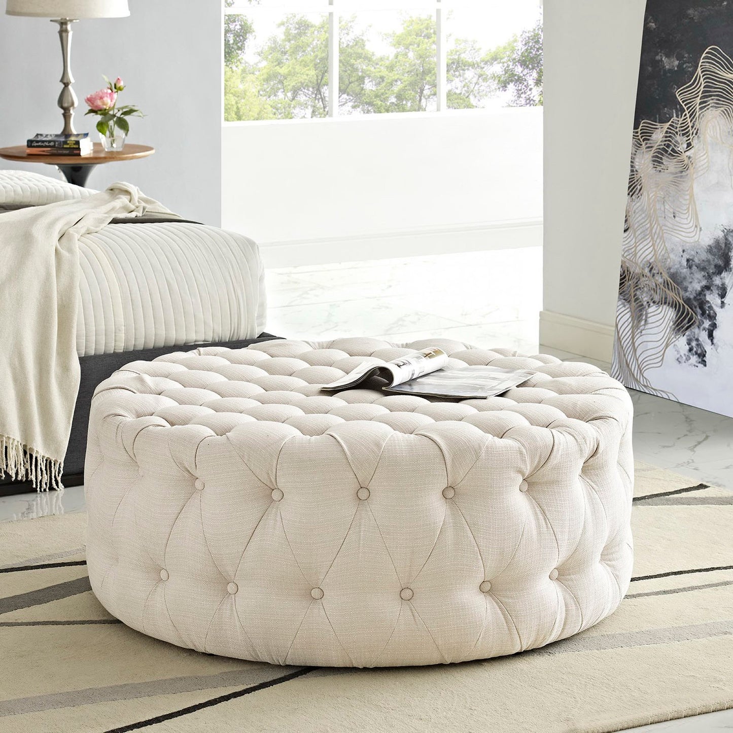 Round brown tufted fabric ottoman with button tufting; plush, versatile footrest or extra seating.