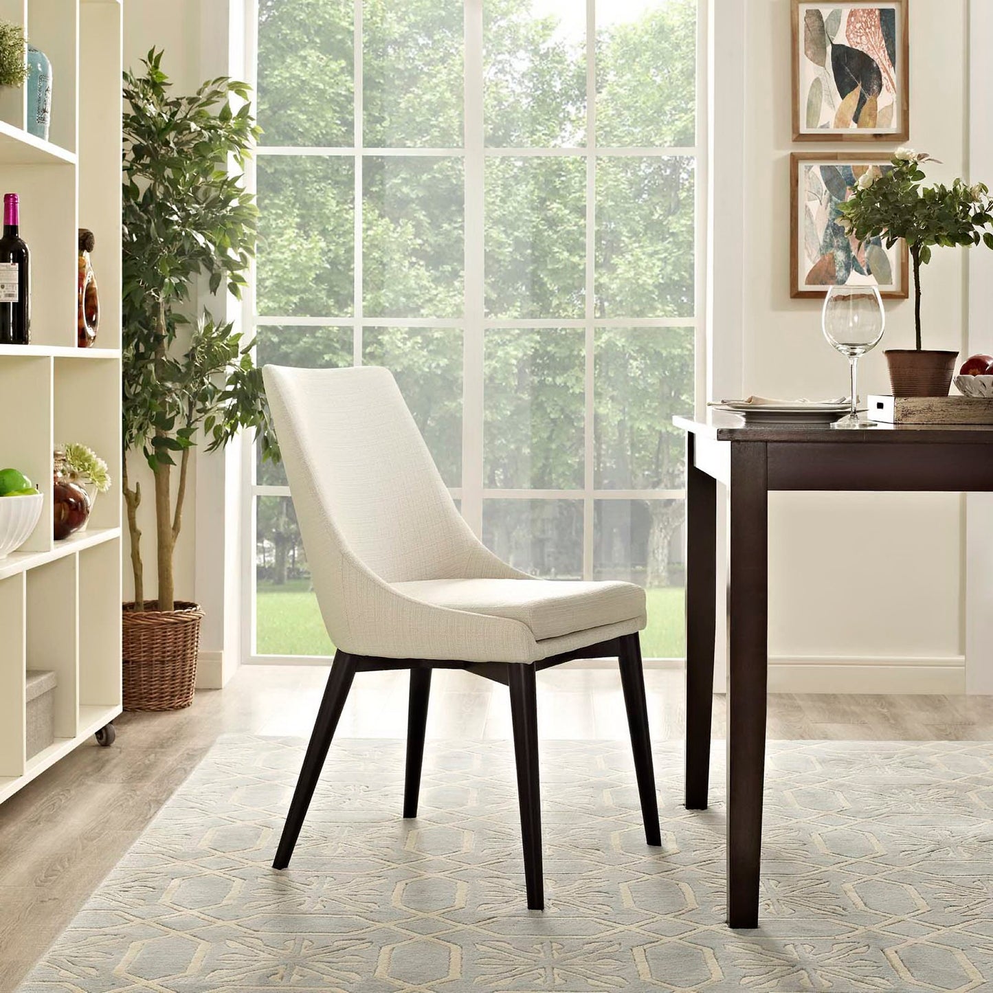 Cream upholstered dining chair with black tapered legs beside a dark wood table in a bright room with windows and plants.