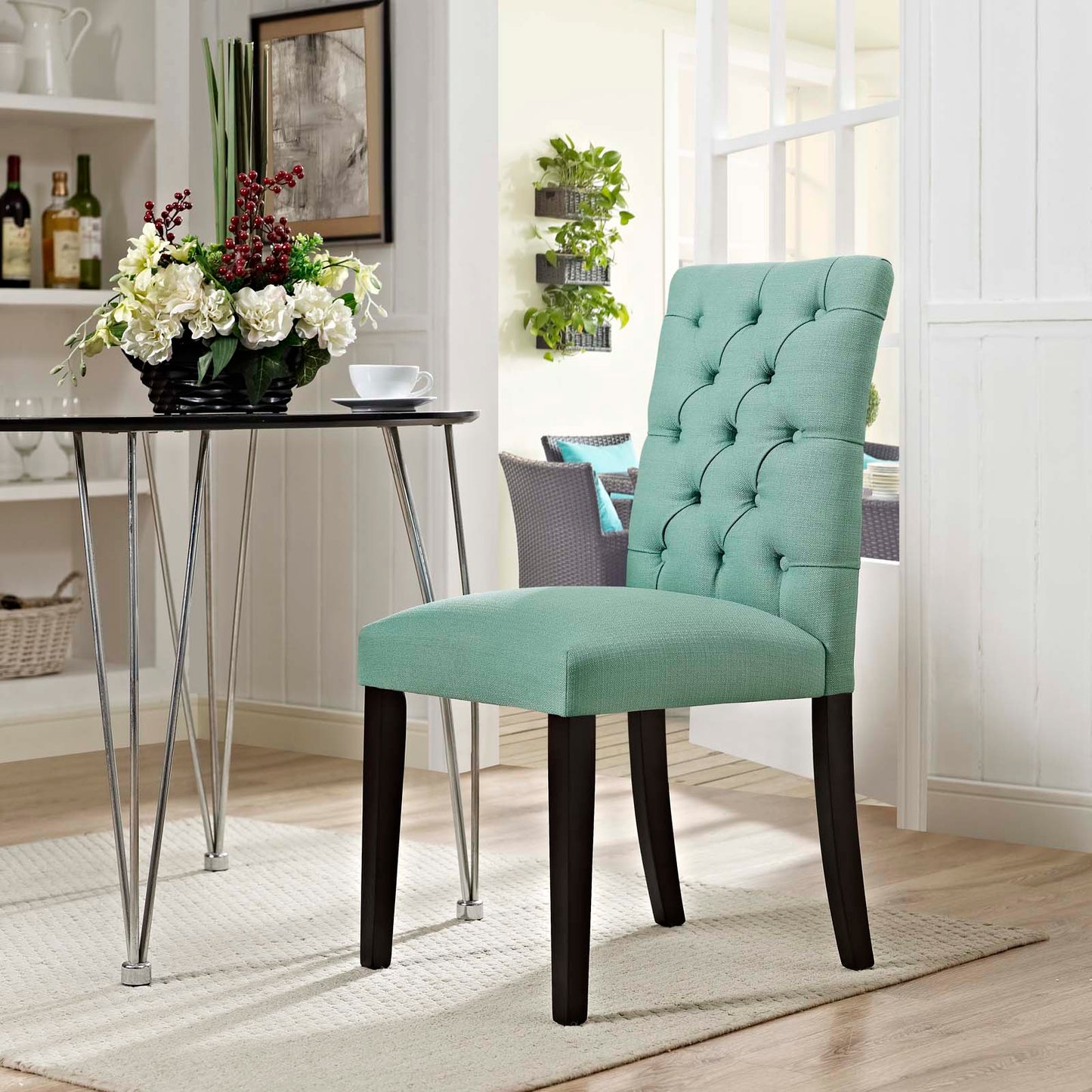 Teal tufted dining chair with padded seat and dark wood legs in a bright, modern dining nook.