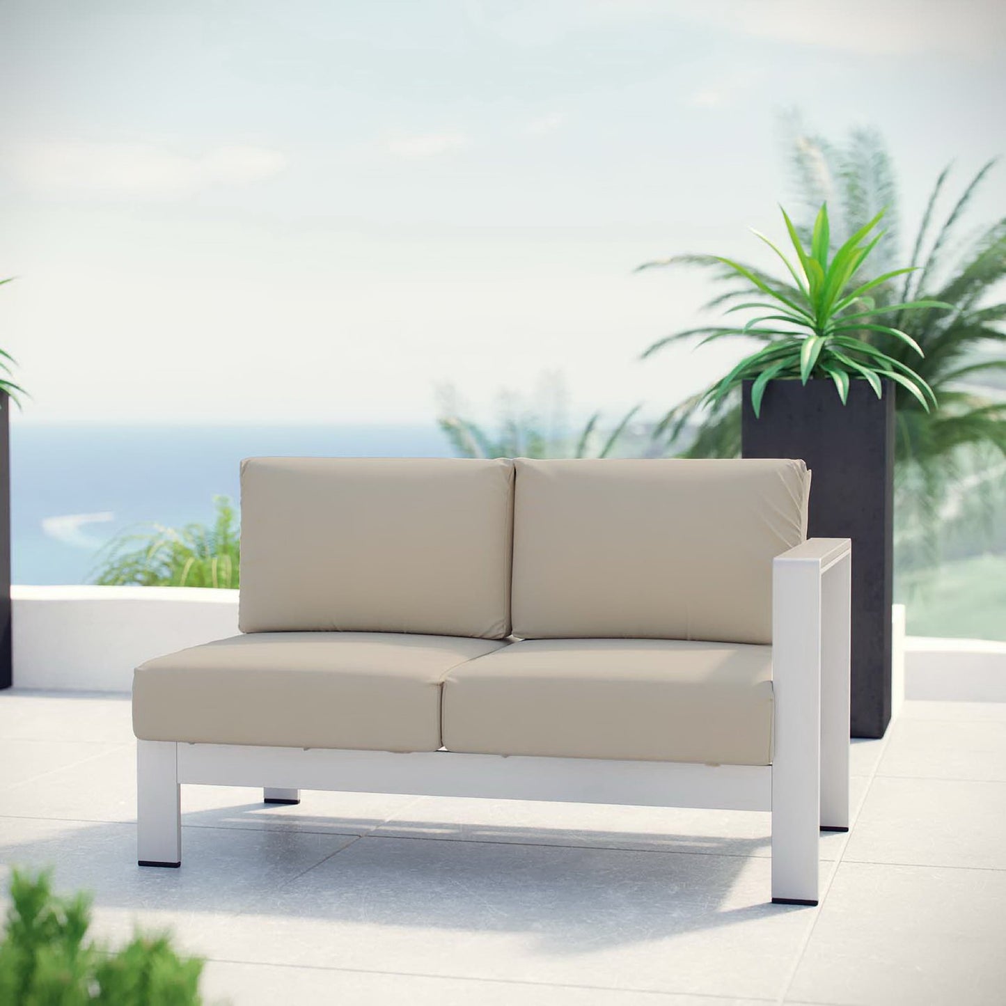 Beige outdoor right-arm corner sectional with aluminum frame and beige cushions on a sunny patio overlooking the sea.