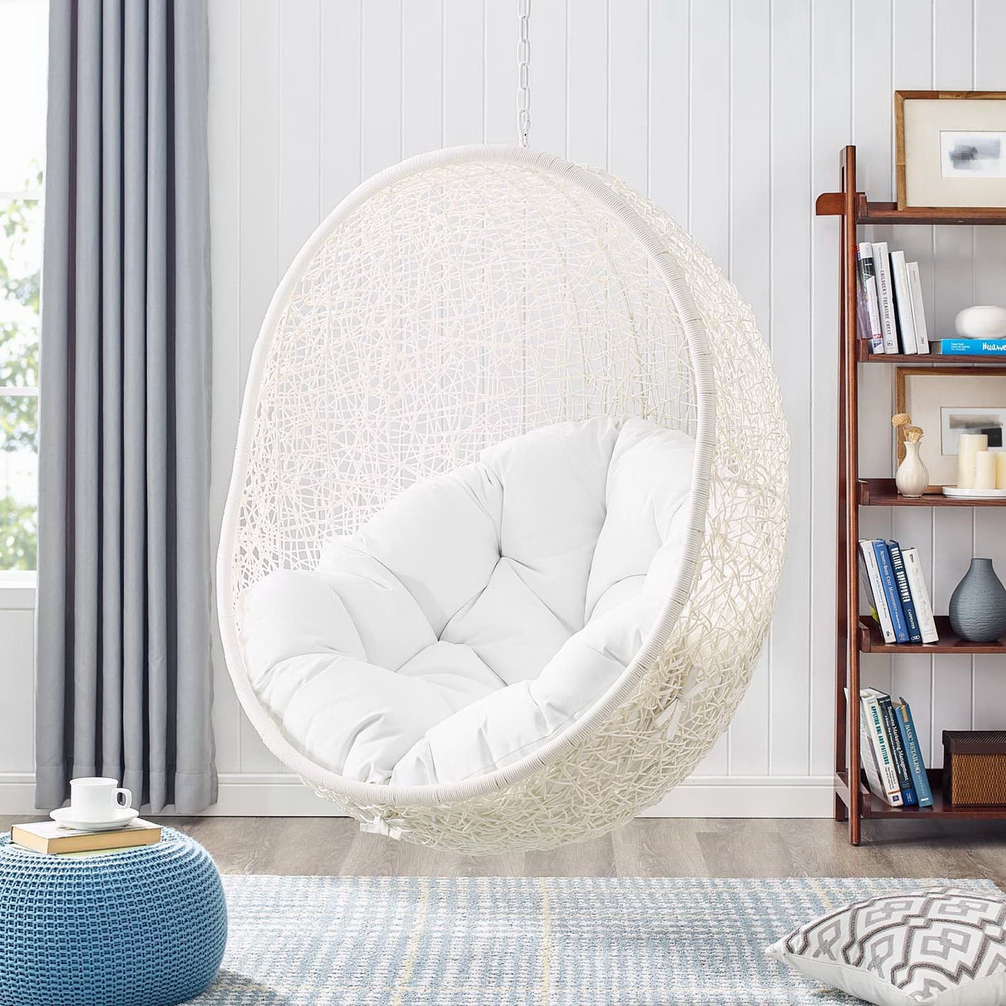 White outdoor patio swing chair with stand and plush cushion in a bright outdoor setting.