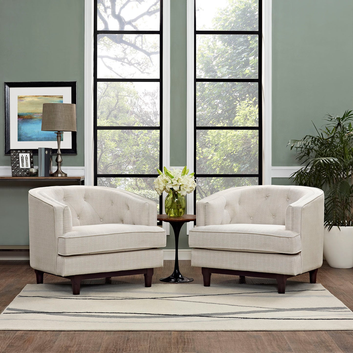 Beige tufted fabric armchairs with dark wood legs flank a round side table with white flowers in a green-walled living room.