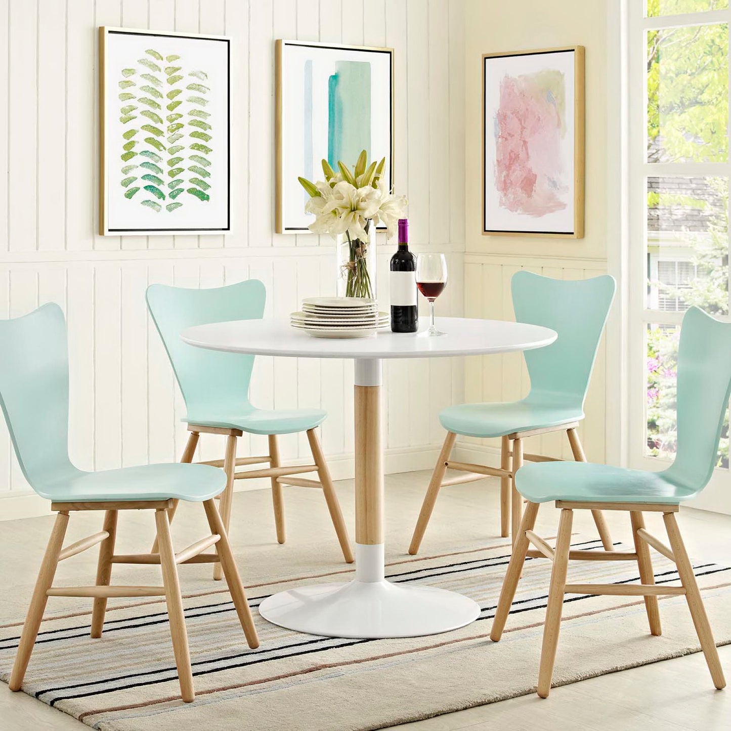 Round white pedestal table with four mint-green mid-century chairs in a sunlit dining nook; vase of white lilies and wine.