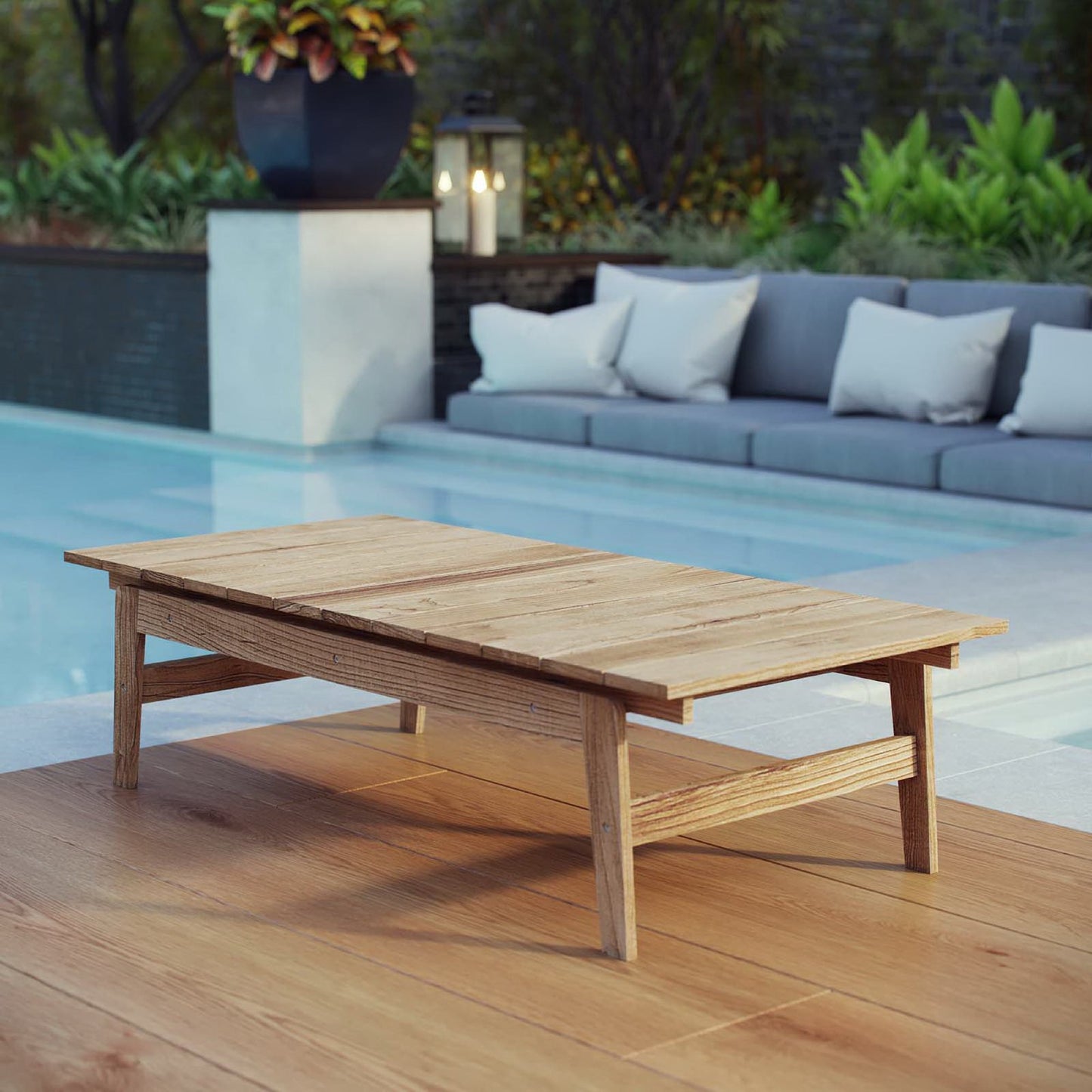 Teak rectangular outdoor coffee table with lower shelf on a pool deck beside a cushioned gray sectional.