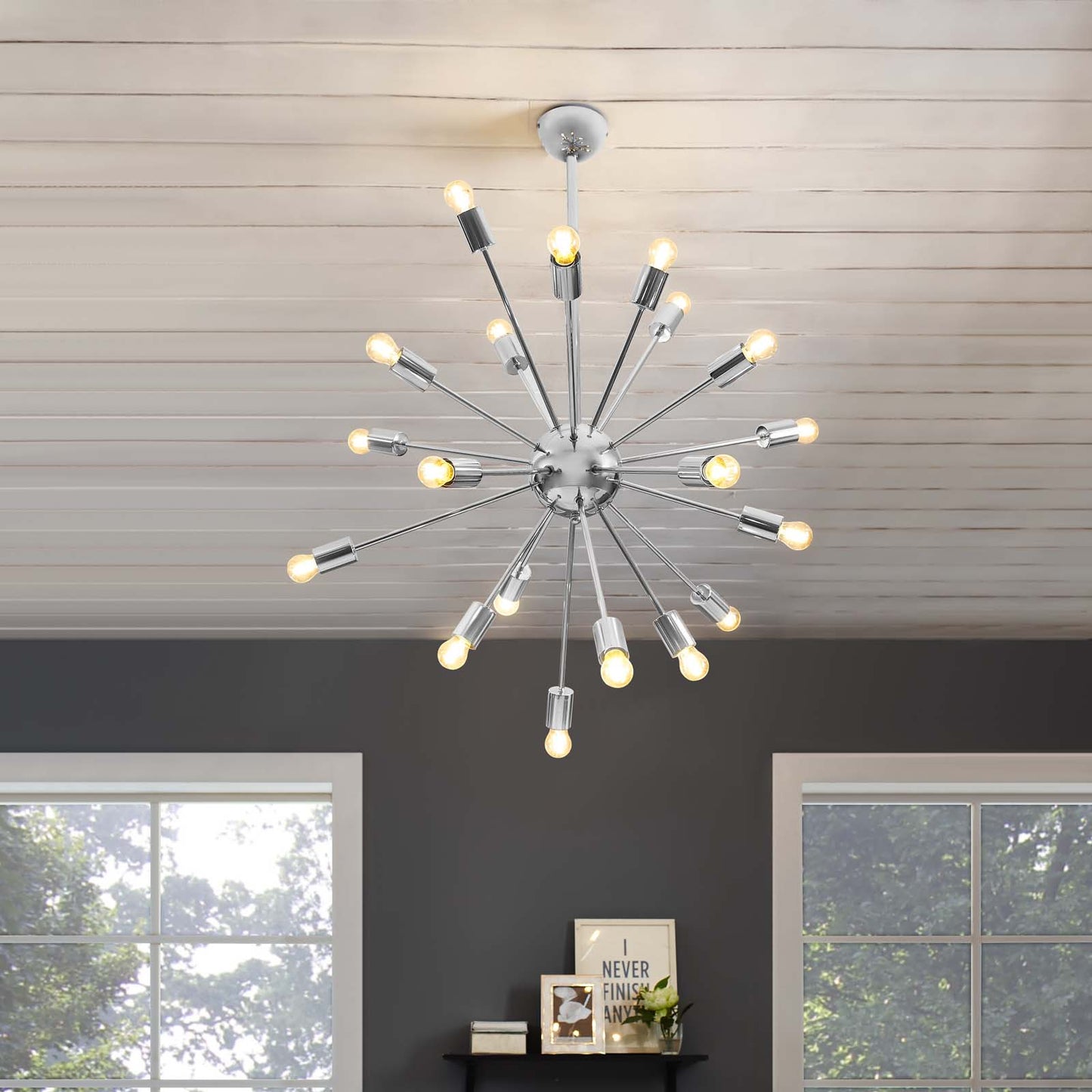 Chrome sputnik chandelier with many radiating arms and exposed warm bulbs over a dark wall in a modern living room.