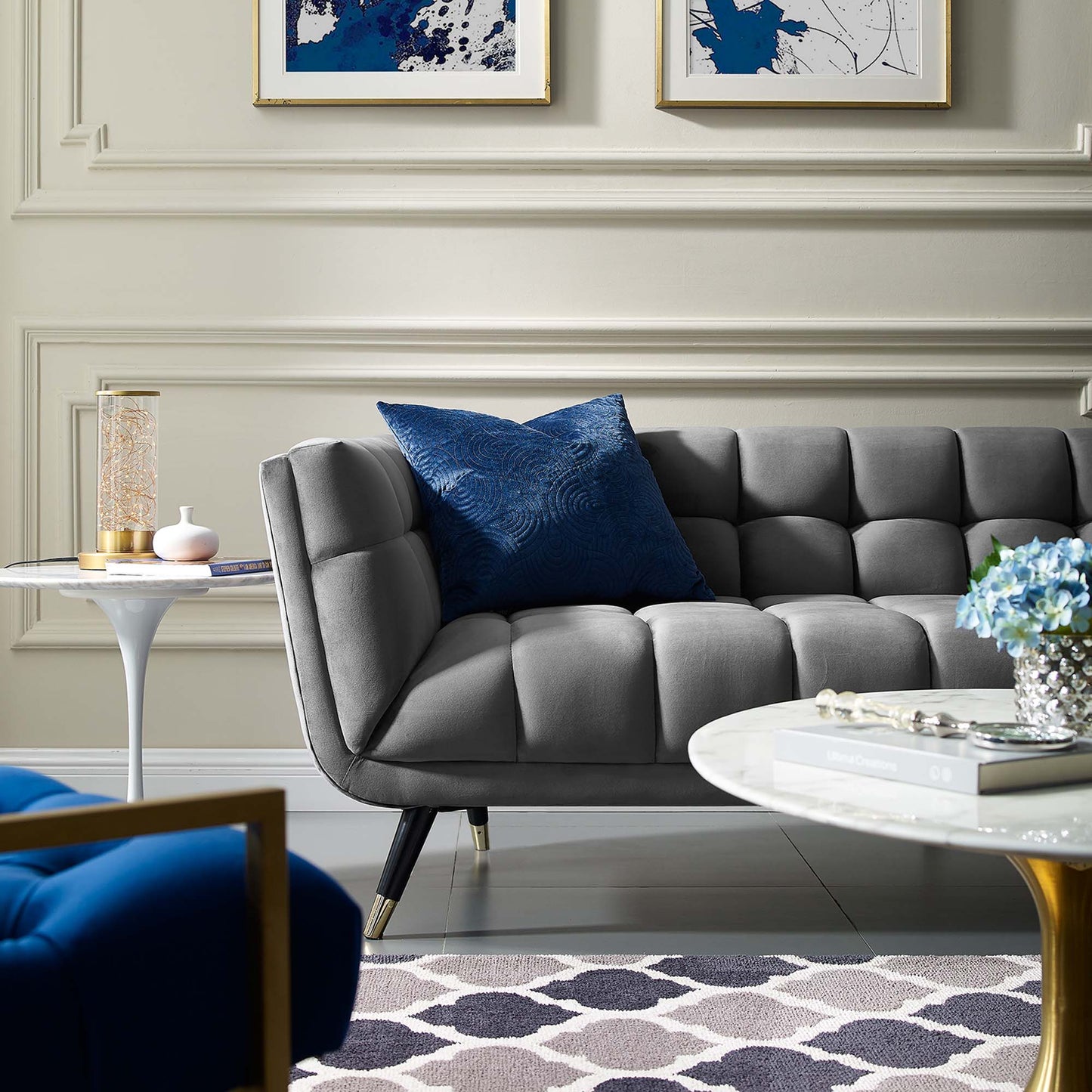 Gray tufted mid-century sofa with blue cushion, gold-leg marble coffee table, blue abstract art in a modern living room.